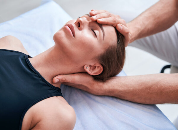 Unrecognized male physiotherapist working with attractive woman in medical office Close up side view portrait of charming young Caucasian female patient lying on massage table while receiving spa treatment in rehabilitation center